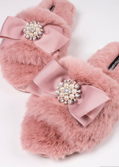 Our Blush Rhinestone Pearl Slippers are perfect to lounge in glamorous style!  The pretty bow topped with rhinestones and pearls sits on top of a faux fur band. This slide style slipper is super comfy with the velvet padded sole.  The non slip grip adds great wearability!