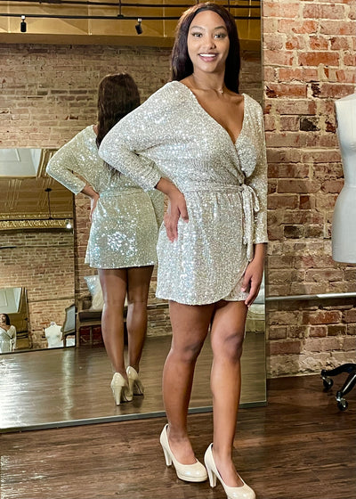 Glitter with every turn in this Gold Sequin Long Sleeve Mini Dress.  Shimmering sequins create shine to this stylish tie-waist wrap dress.