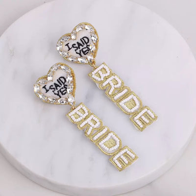 The “I Said Yes” Beaded Earrings are such a fun way to let everyone know the good news!!  Handcrafted with white and gold beads, “Bride” dangles from a heart  surrounded by rhinestones.  