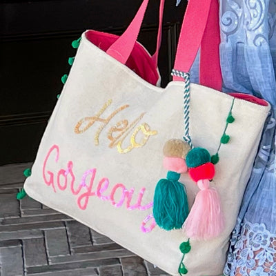 “Hello Gorgeous” Canvas And Sequin Tote Bag With Tassel. This fun canvas woven tote bag is detailed with sequin calligraphy.  It is certain necessity for your next beach trip or even bachelorette weekend!